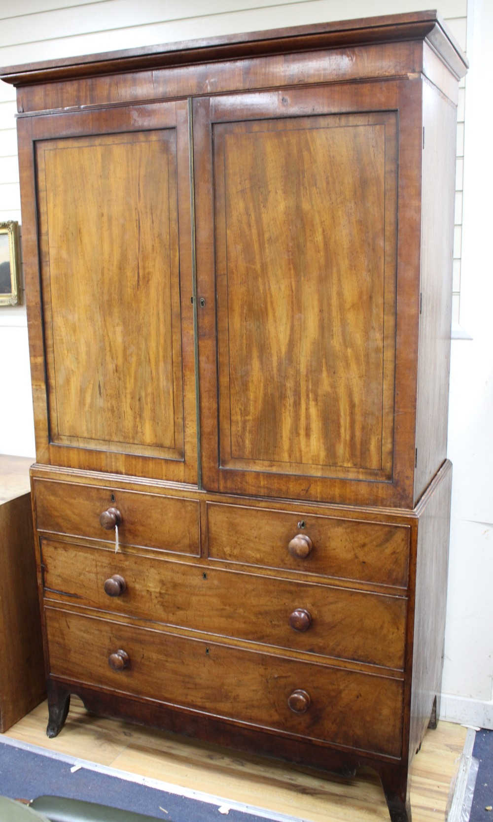 A Regency mahogany linen press with two doors enclosing five slides, two short drawers and two graduated long drawers, on swept bracket